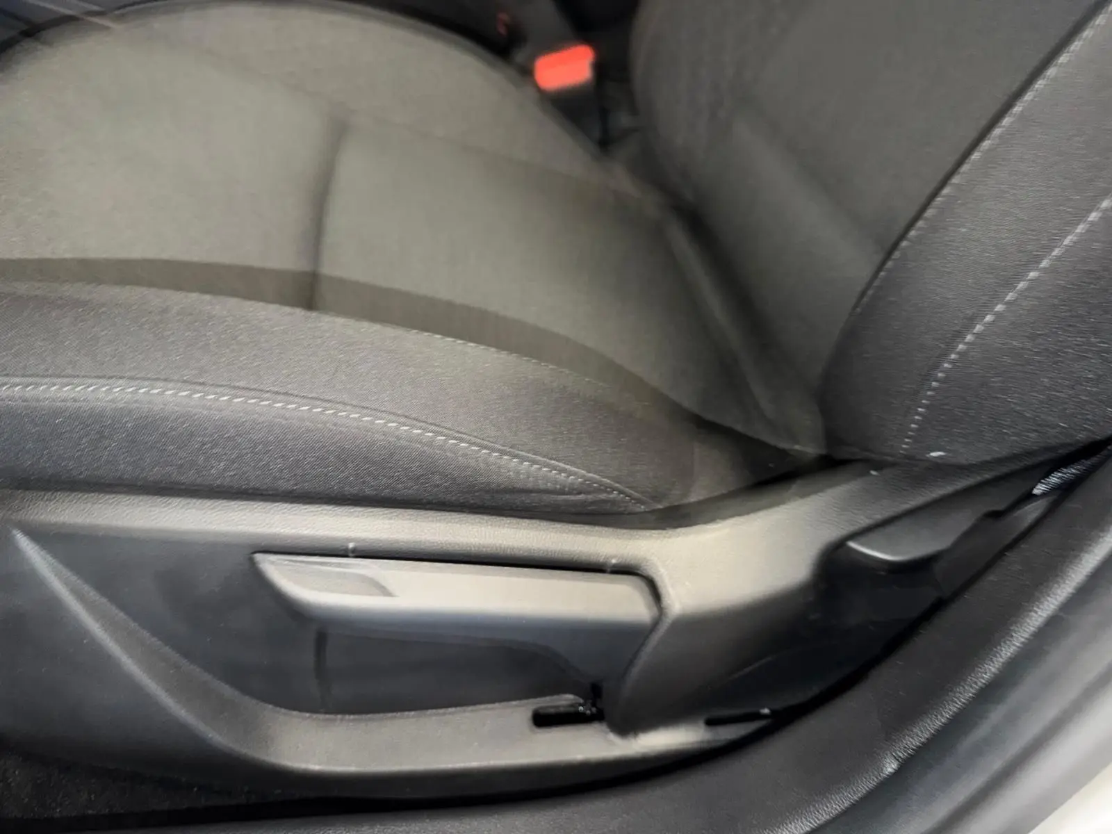 Gros plan sur le réglage manuel du siège conducteur en tissu gris dans une Renault Clio 2023, côté gauche.