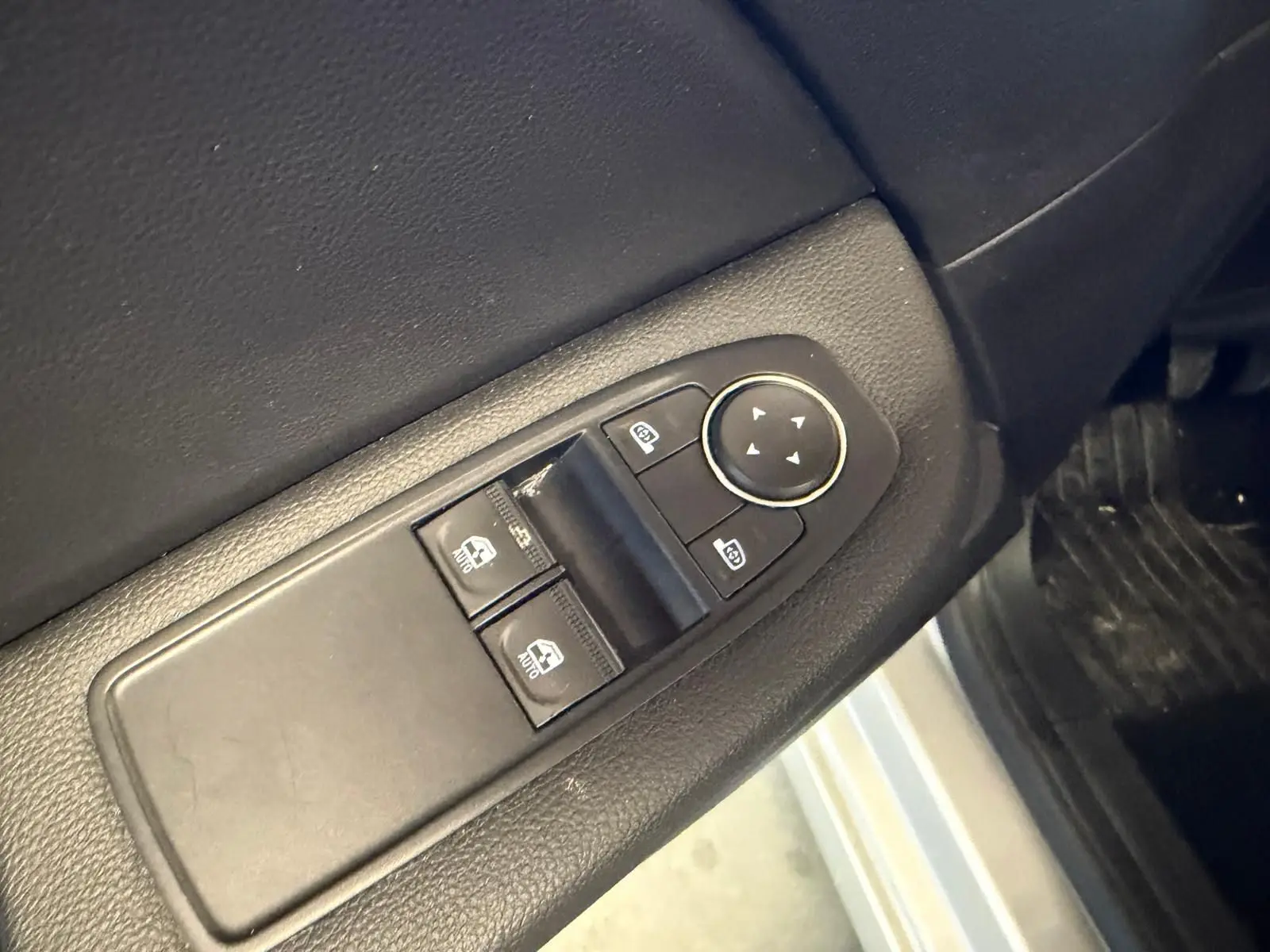Gros plan sur les commandes de vitres électriques et rétroviseurs côté conducteur d’une Renault Clio gris platine.