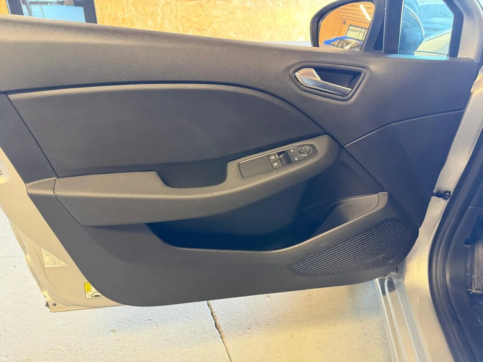 Vue intérieure côté gauche de la porte avant gris platine de la Renault Clio 2023 avec commandes de vitres électriques.