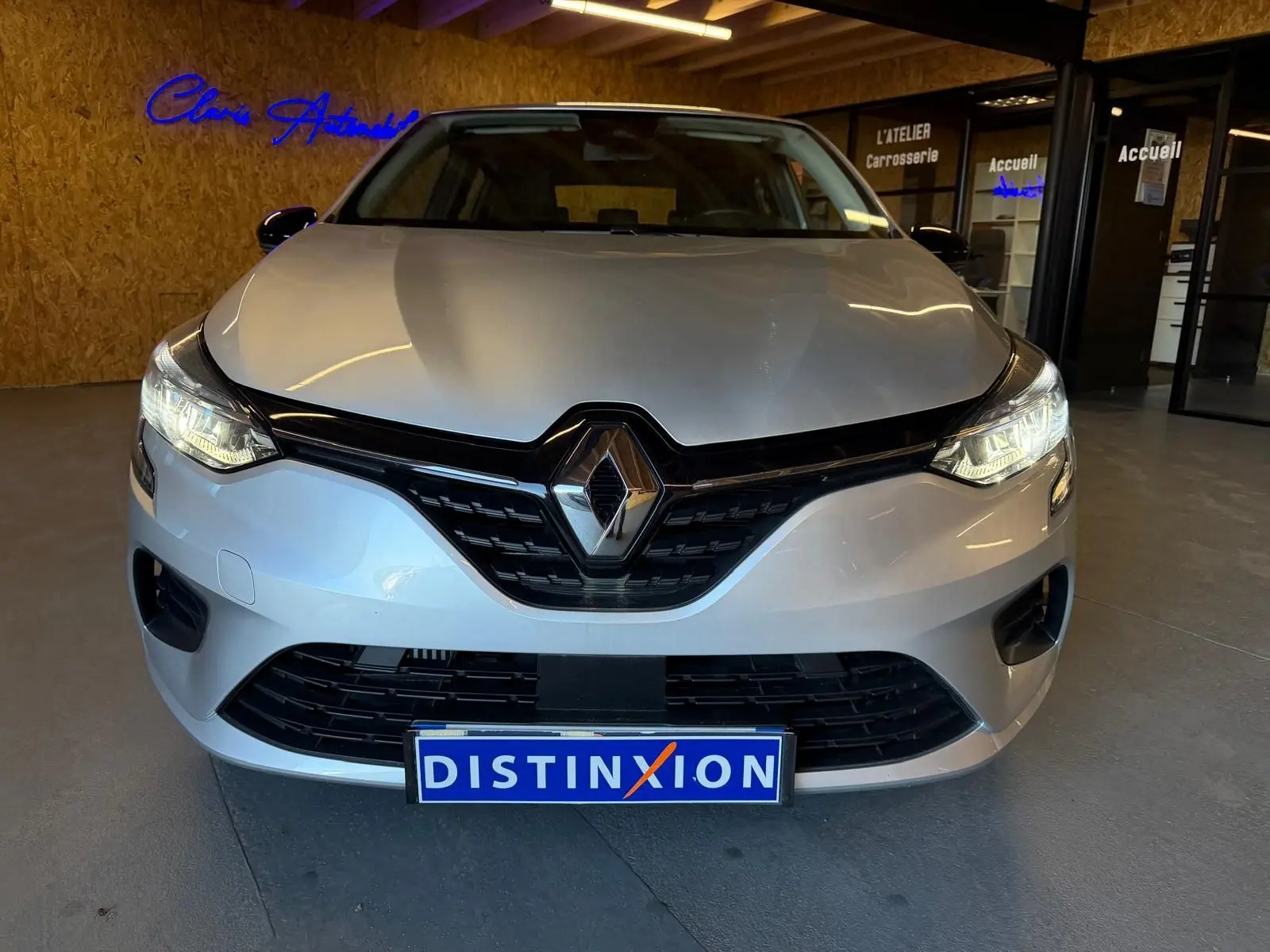 Vue avant d'une Renault Clio 1.0 TCE 90 Équilibre gris platine avec phares allumés en intérieur showroom.