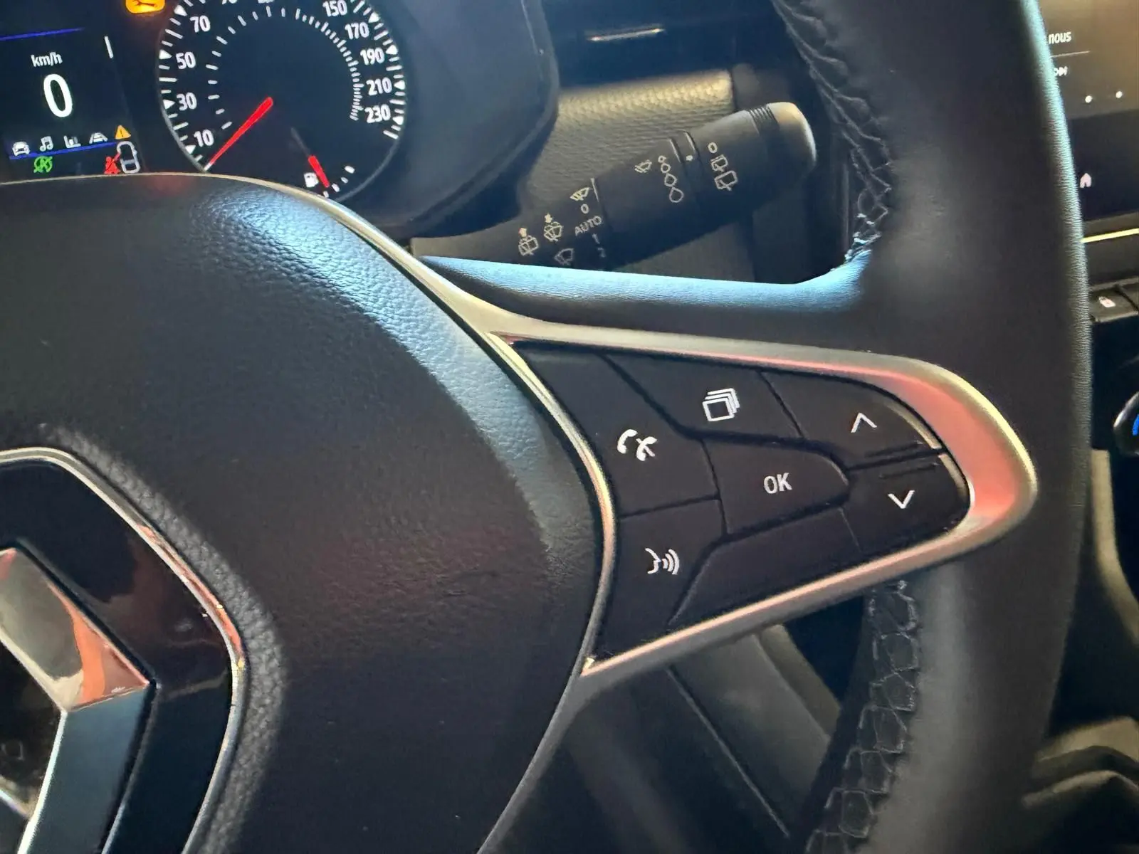 Gros plan sur le volant noir de la Renault Clio 2023 avec commandes multifonctions et tableau de bord partiel en arrière-plan.