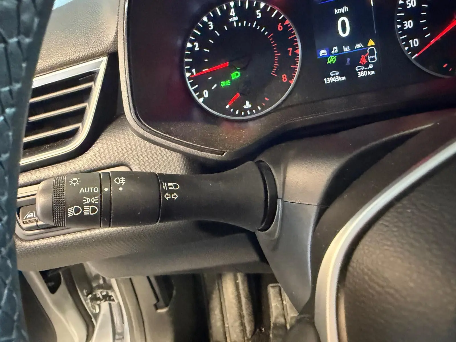 Vue rapprochée du commodo des feux et clignotants sur le volant noir d'une Renault Clio gris platine 2023.