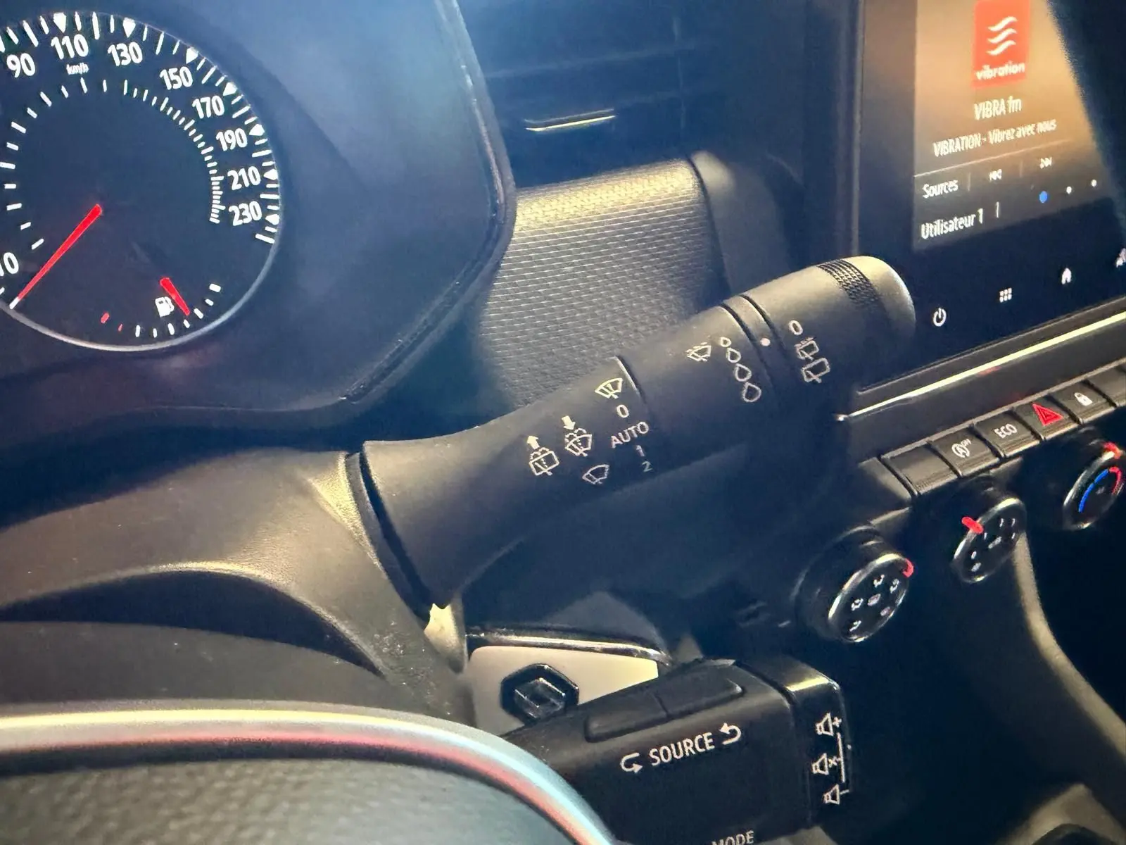 Détail intérieur du tableau de bord côté gauche de la Renault Clio gris platine 2023, avec commandes essuie-glaces et écran tactile.