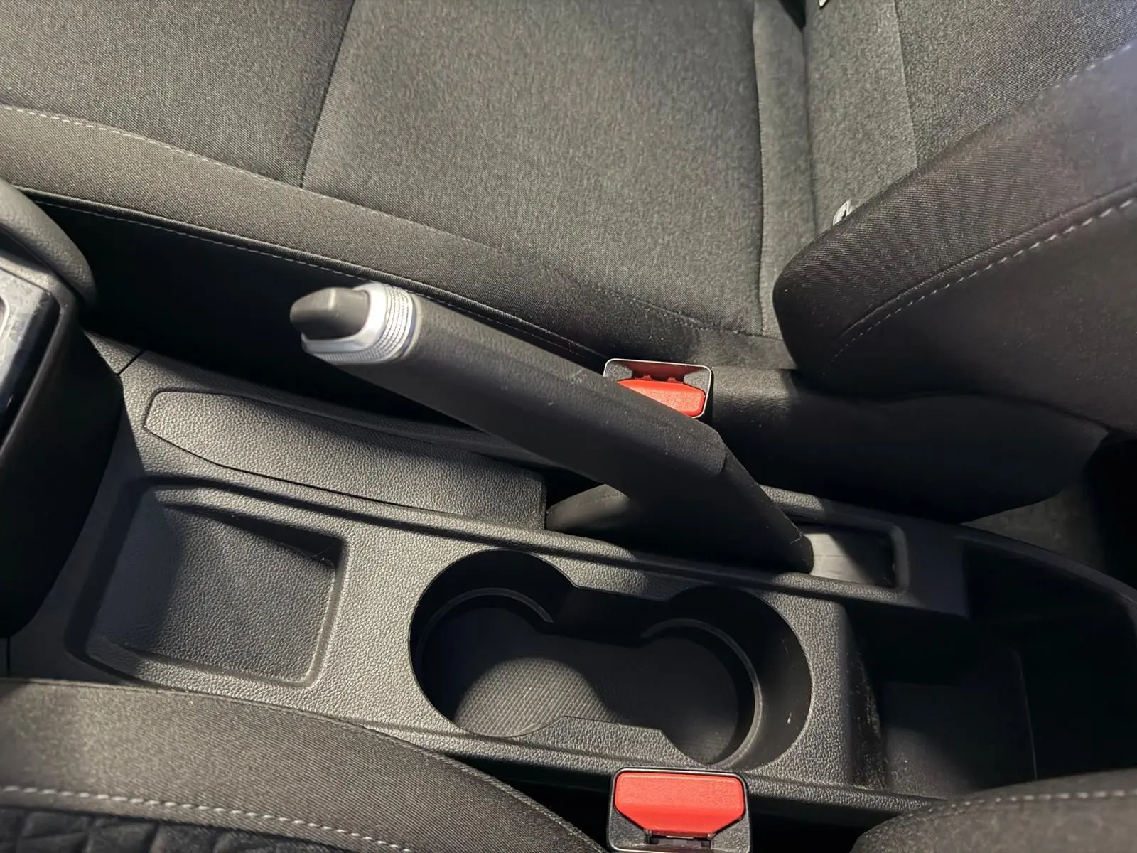 Vue en plongée sur le frein à main et porte-gobelets noirs entre les sièges avant d'une Renault Clio gris platine.