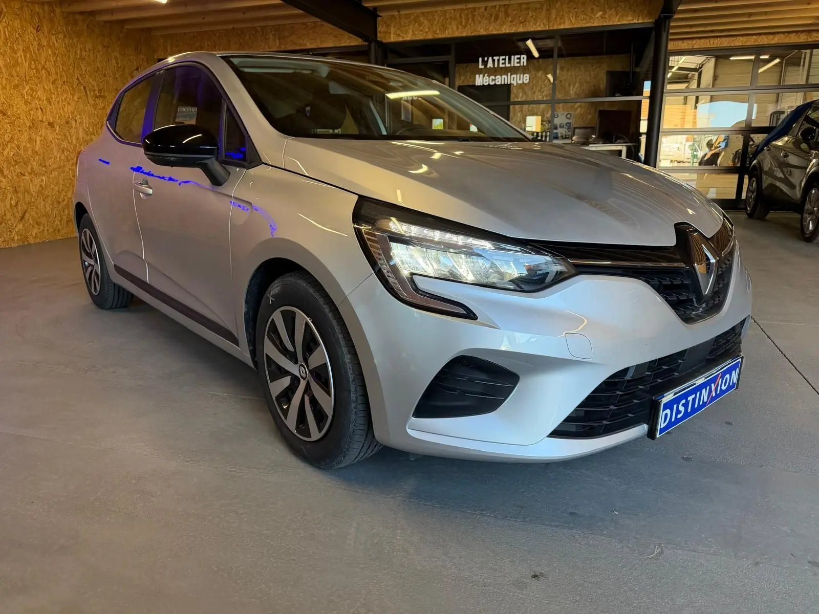 Renault Clio gris platine vue 3/4 avant droit en intérieur avec phares LED et jantes stylisées.