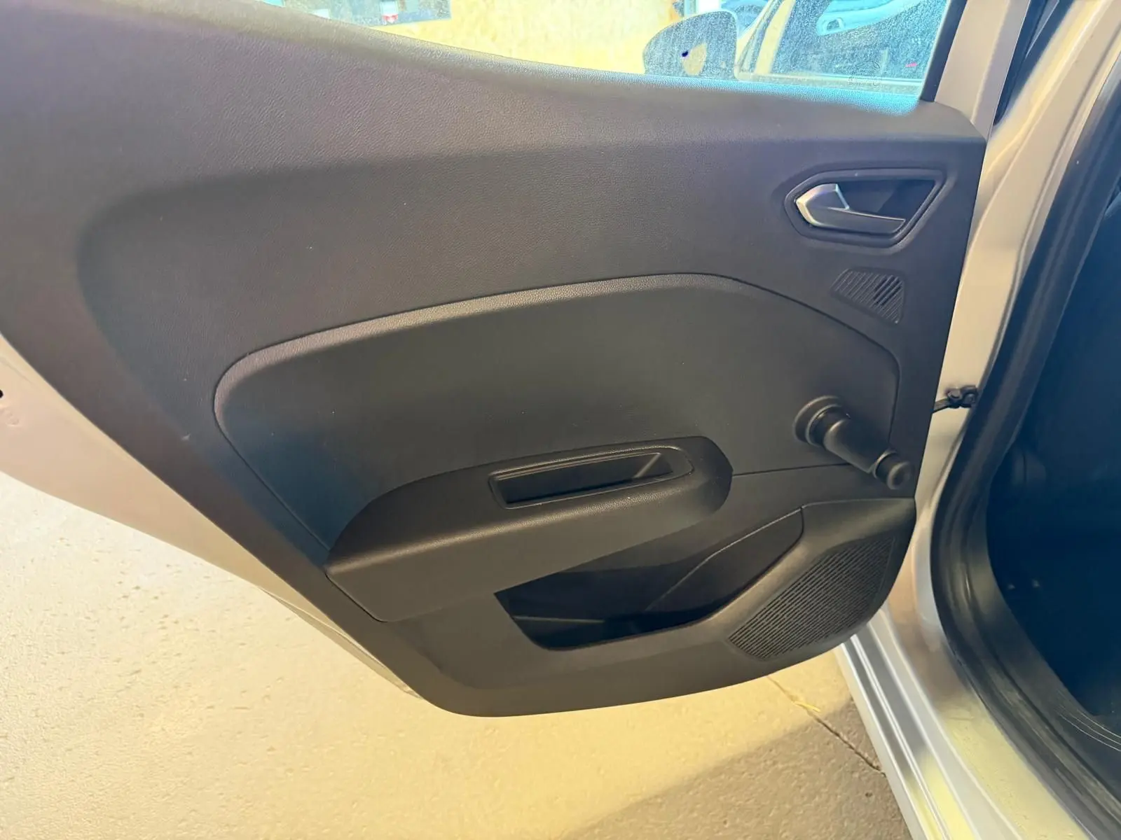 Vue rapprochée de la porte arrière gauche ouverte d'une Renault Clio gris platine, avec poignée et manivelle de vitre noire.