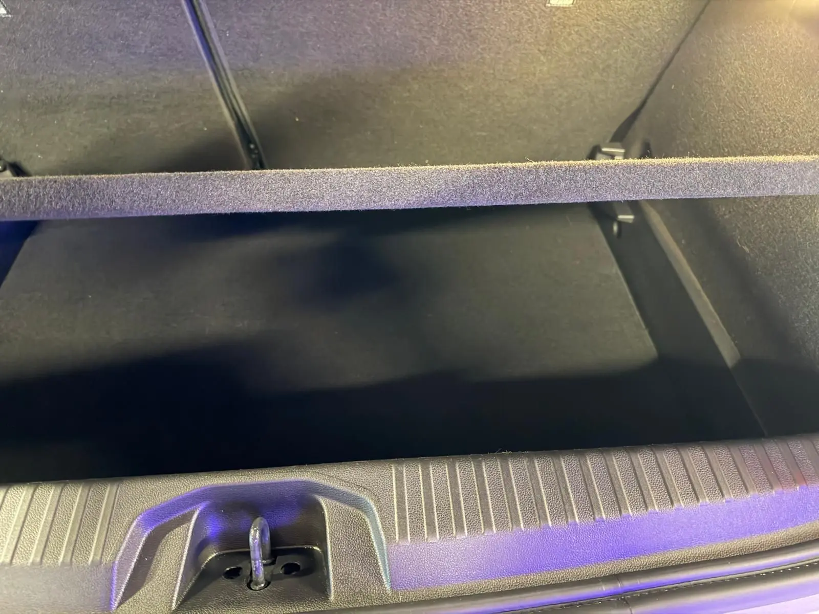 Vue intérieure du coffre ouvert de la Renault Clio gris platine, montrant la plage arrière et le tapis de coffre noir.