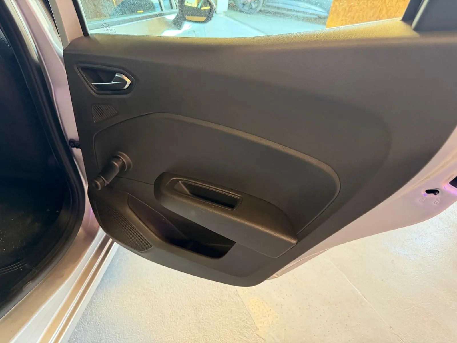 Vue rapprochée de la porte arrière gauche noire de la Renault Clio gris platine, avec poignée et manivelle de vitre.