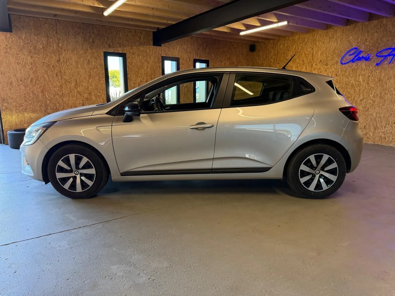 Profil côté gauche d'une Renault Clio 1.0 TCE 90 Équilibre gris platine, avec jantes et becquet arrière visible en intérieur.