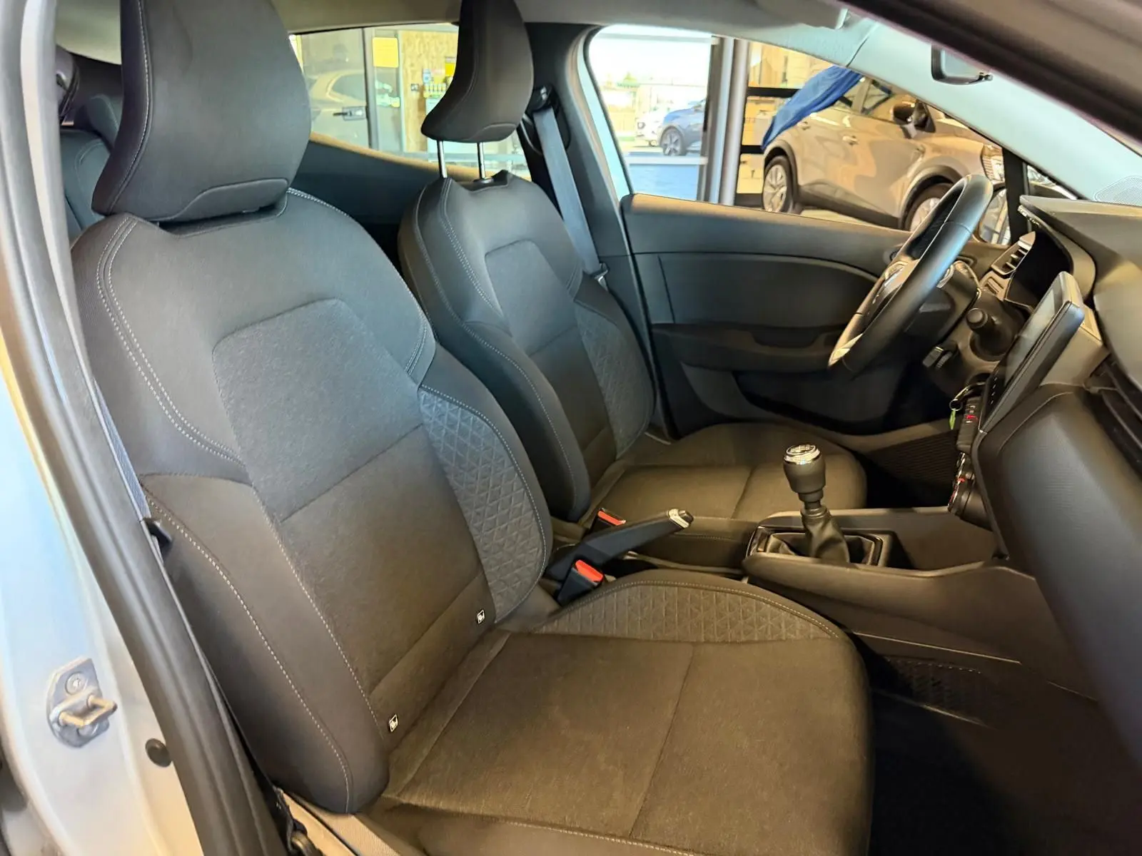 Vue intérieure côté conducteur de la Renault Clio 2023, sièges noirs avec coutures contrastées et levier de vitesse manuel.