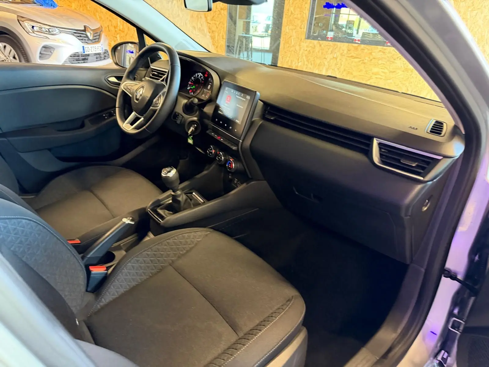 Vue intérieure côté conducteur de la Renault Clio gris platine 2023 avec tableau de bord et écran tactile.