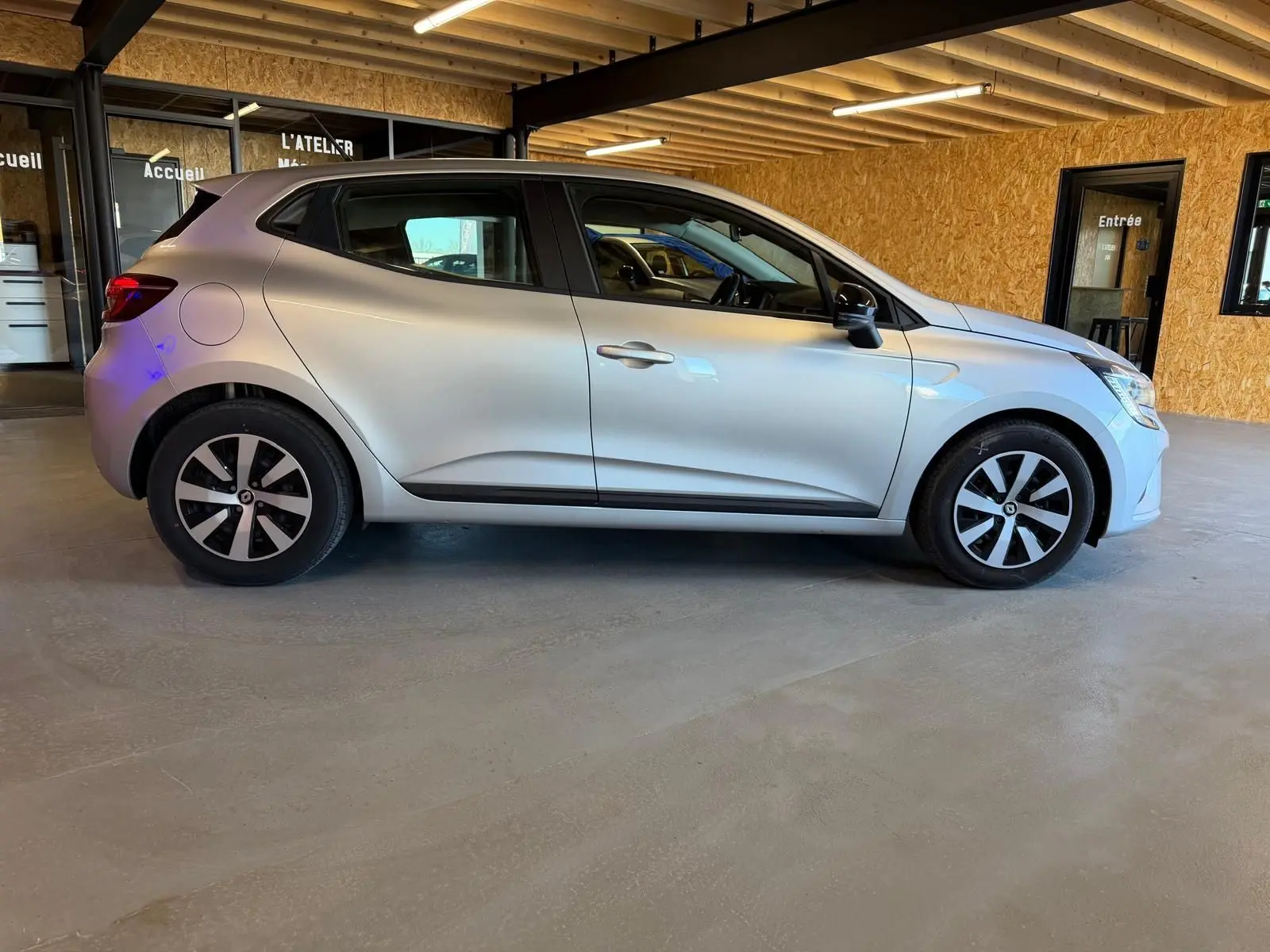 Profil droit d'une Renault Clio gris platine 2023, avec enjoliveurs noirs et poignées ton carrosserie visibles.