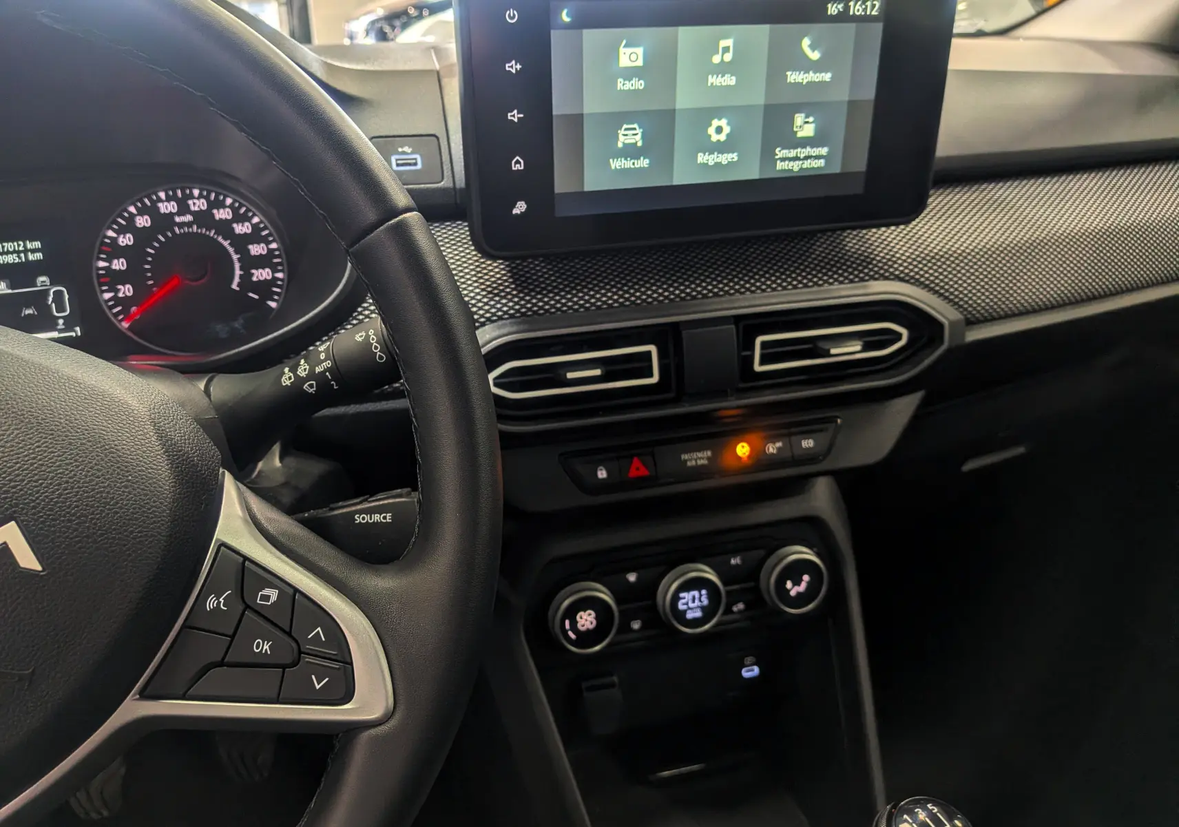 Vue intérieure côté conducteur du tableau de bord gris schiste de la Dacia Sandero 2025 avec écran tactile et commande manuelle.