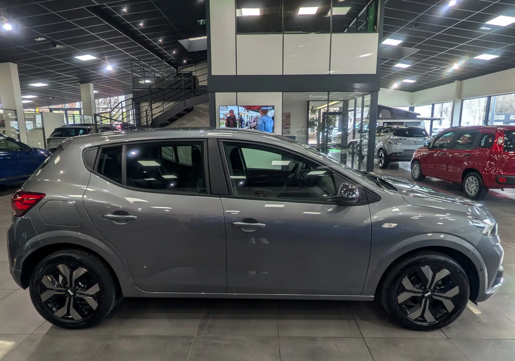 Profil côté droit d'une Dacia Sandero TCe 90 CH Journey gris schiste, avec jantes alliage et intérieur visible en concession.