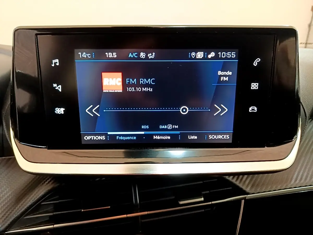 Écran tactile central du tableau de bord du Peugeot 2008 blanc, affichant la radio FM RMC à 103,10 MHz.