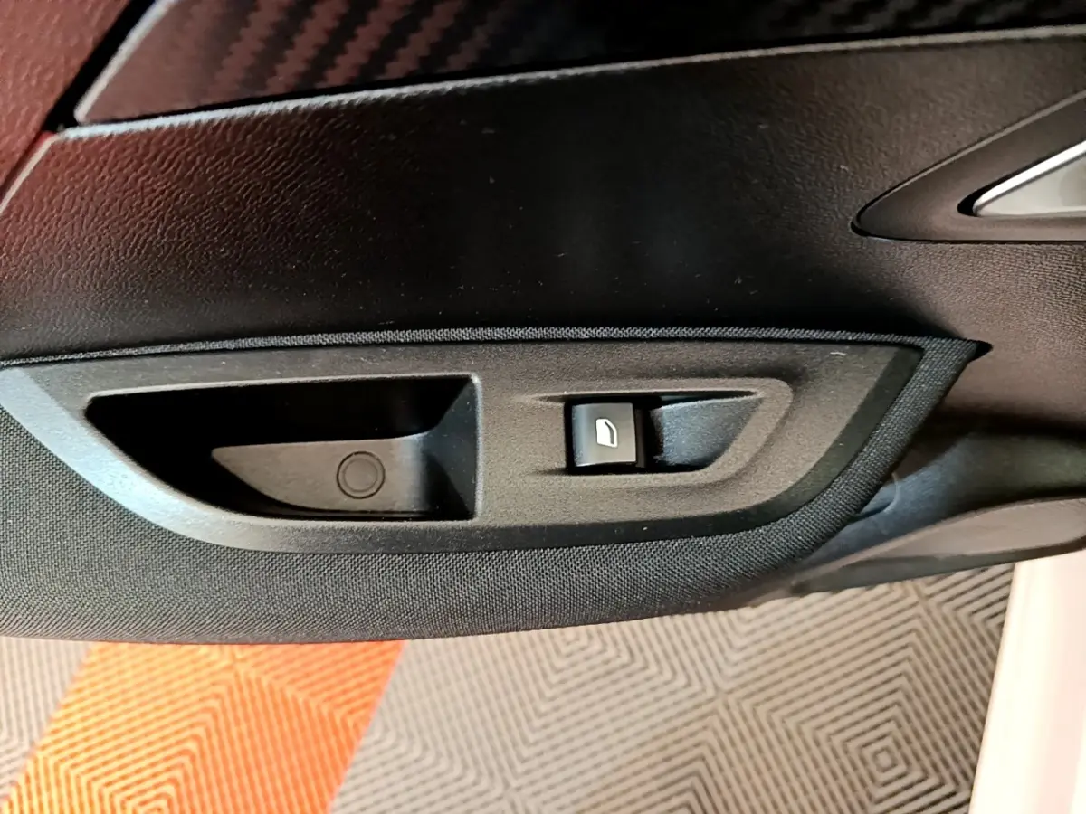 Gros plan sur la commande d’ouverture de coffre côté intérieur d’une Peugeot 2008 blanche, avec habillage noir.