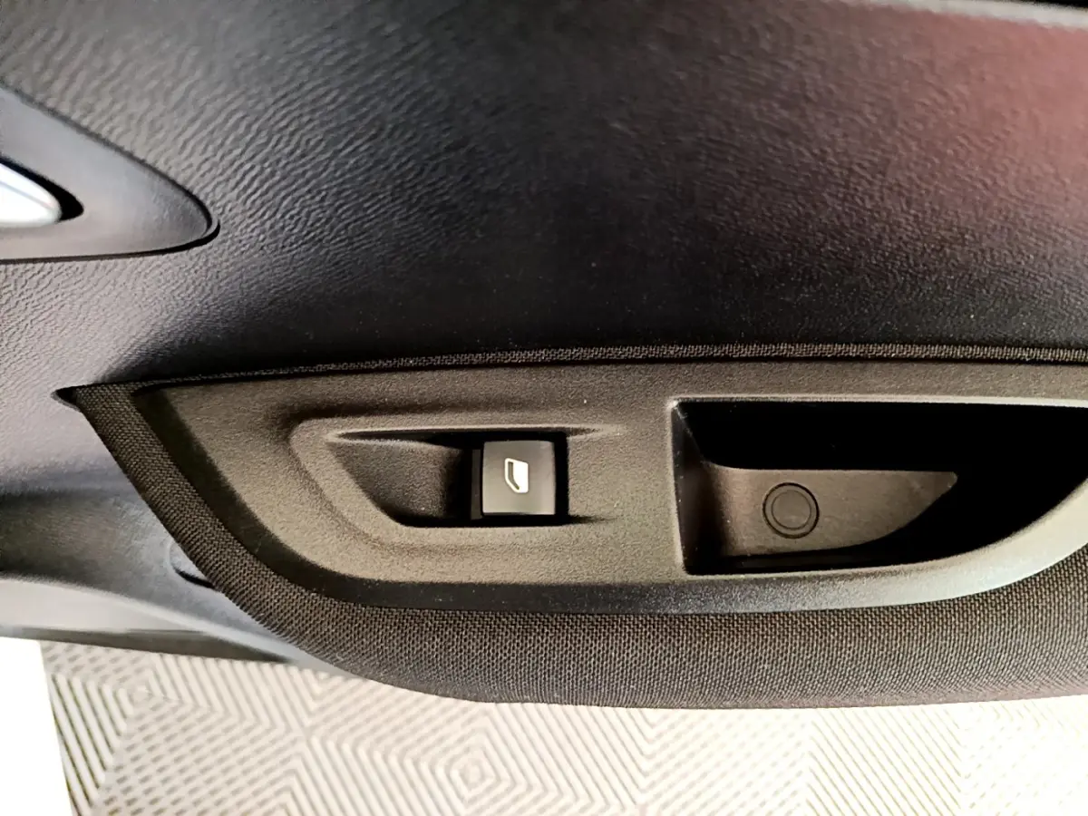 Gros plan sur le bouton d'ouverture de coffre intégré dans le panneau intérieur noir d'une Peugeot 2008 blanche.