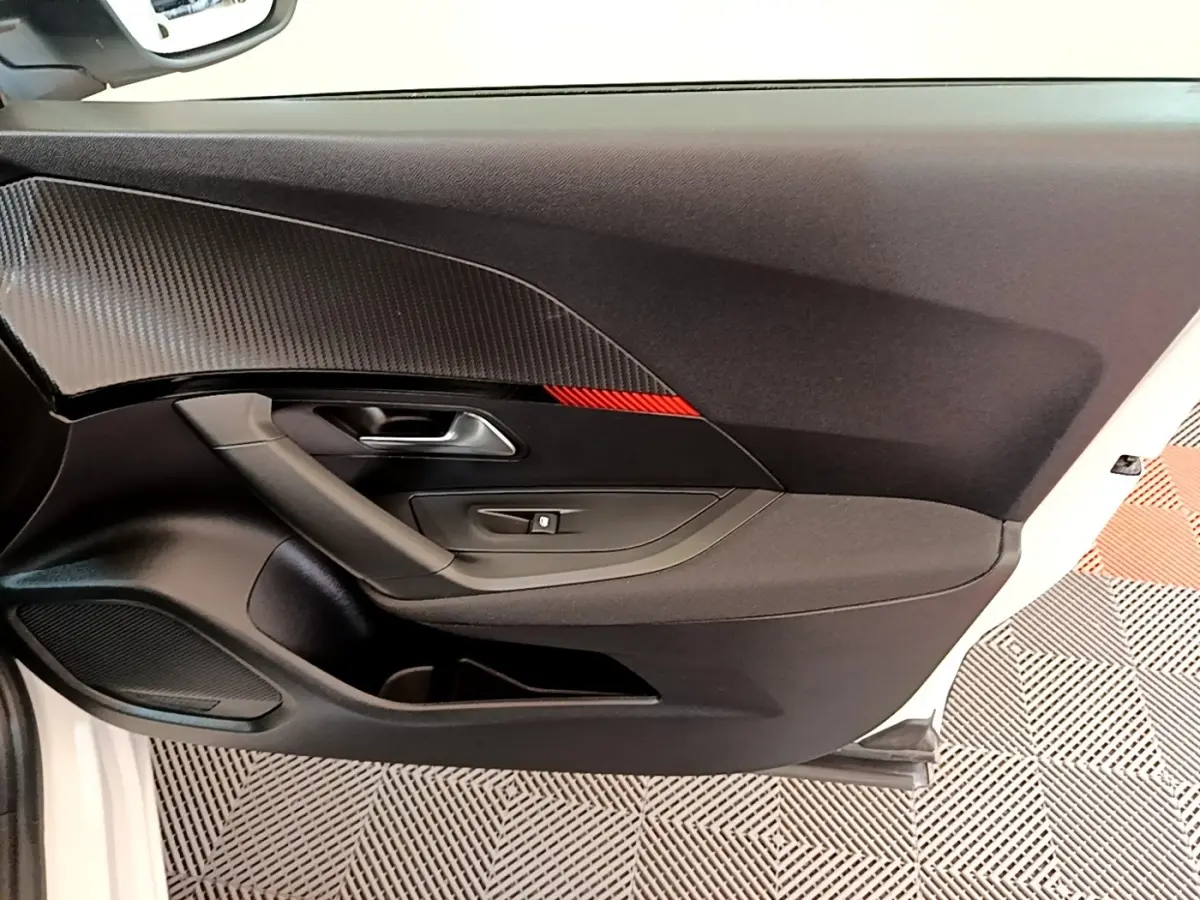 Vue intérieure de la porte côté conducteur d’un Peugeot 2008 blanc, avec insert noir texturé et bande rouge.