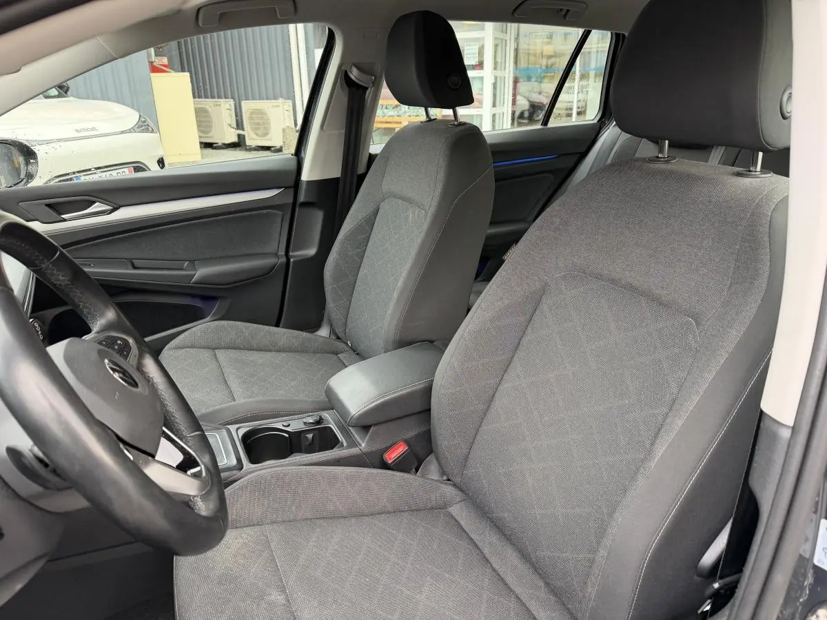 Vue intérieure côté avant gauche de la Volkswagen Golf SW 2.0 TDI gris avec sièges tissu Maze et accoudoir central.