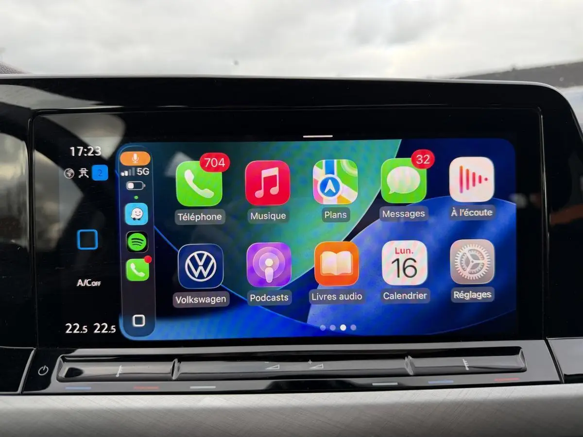 Écran tactile central affichant l'interface Apple CarPlay dans une Volkswagen Golf gris, vue de face intérieure.