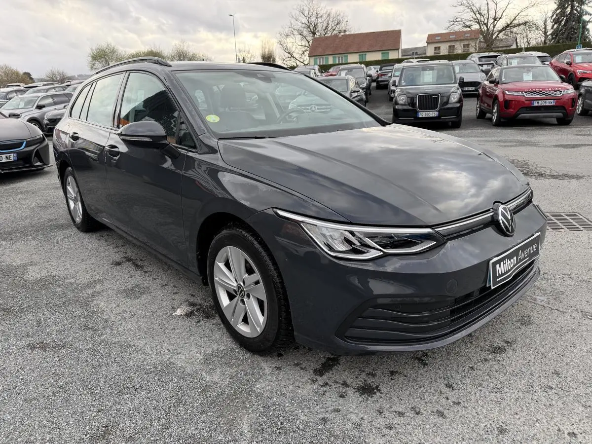 Volkswagen Golf SW gris vue 3/4 avant droit, jantes alliage et calandre épurée sous ciel nuageux.
