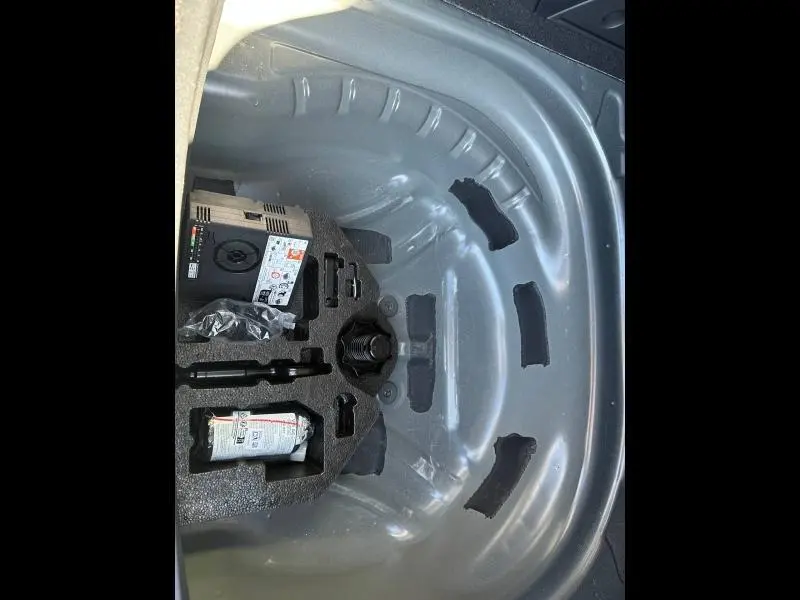 Coffrage de rangement sous le coffre d'une SEAT LEON ST 2025, contenant une bombe de réparation et un compresseur, vue plongeante.