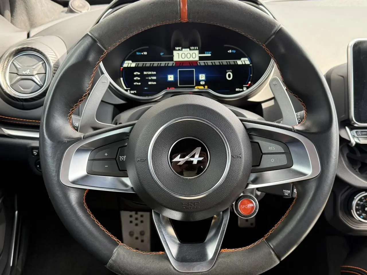 Vue rapprochée du volant noir avec surpiqûres orange et tableau de bord numérique de l'Alpine A110 Gris Tonnerre Mat.