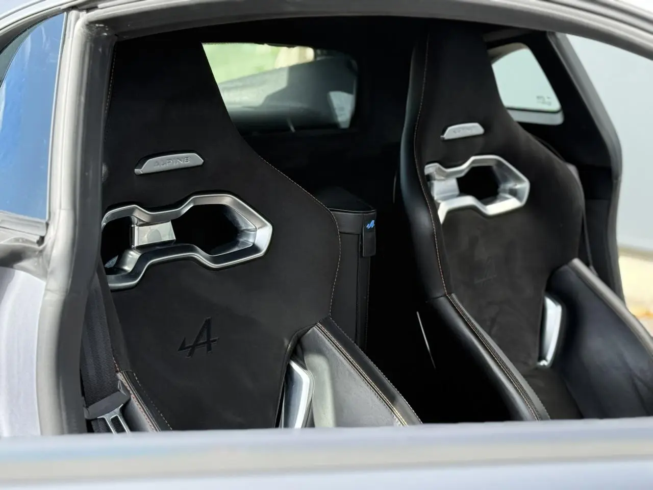 Vue intérieure rapprochée des sièges baquets noirs Alpine A110 1.8T 292 S avec surpiqûres orange et détails métalliques.