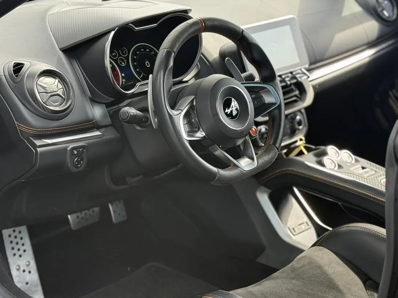 Vue intérieure côté conducteur de l'Alpine A110 1.8T 292 S 2020, volant cuir noir avec surpiqûres orange et tableau de bord moderne.