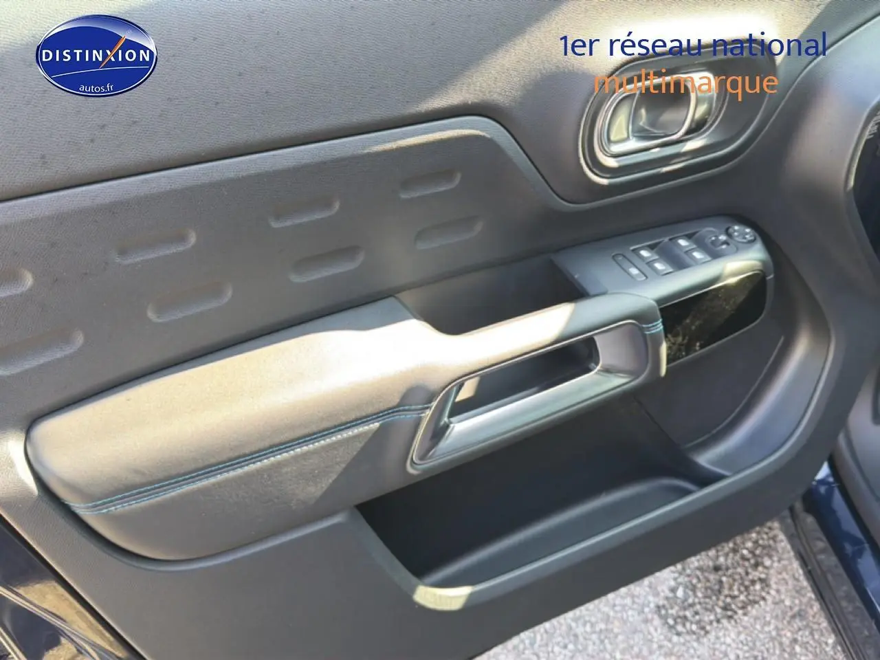 Vue intérieure côté gauche de la porte avant d’un Citroën C5 Aircross bleu eclipse avec commandes de vitres et poignée intégrée.