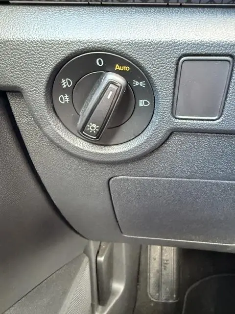 Gros plan sur le bouton de commande des feux avec mode automatique dans l’habitacle gris foncé du Volkswagen T-Cross 2023.