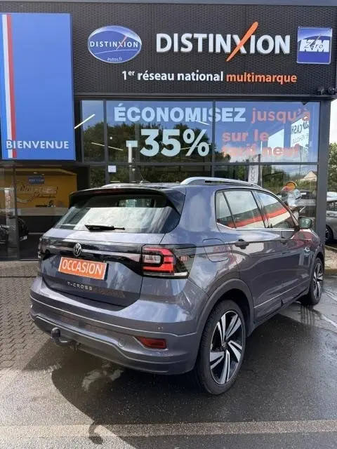 Vue 3/4 arrière droite d'un Volkswagen T-Cross gris foncé 2023 avec finition R-Line devant un concessionnaire multimarque.