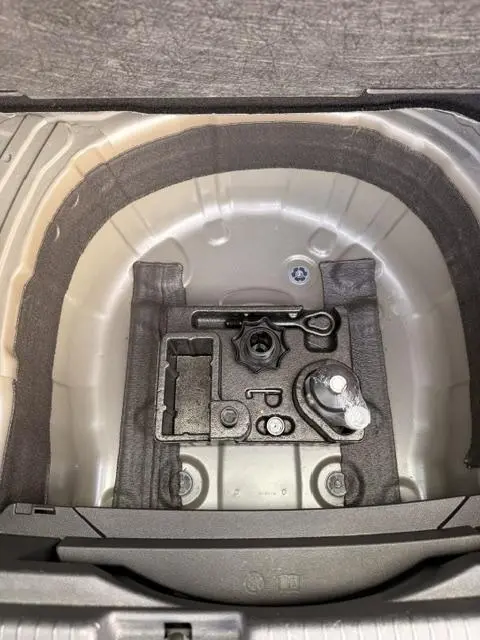 Vue en plongée sur le coffre gris foncé du Volkswagen T-Cross 2023, montrant le rangement d’outils et l’emplacement de la roue de secours.