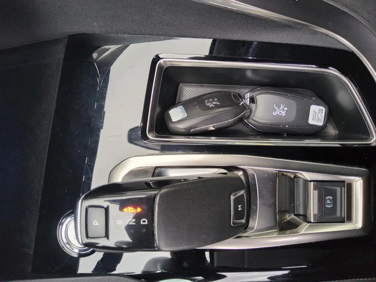 Gros plan sur la console centrale noire brillante du Peugeot 3008 2019 avec levier de boîte auto et clés.