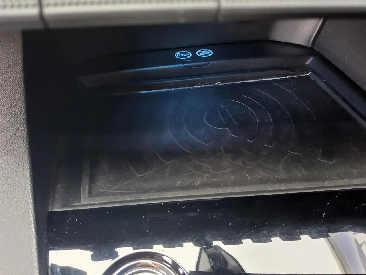 Surface de recharge sans fil noire dans l'habitacle du Peugeot 3008 rouge foncé, vue rapprochée du compartiment central.