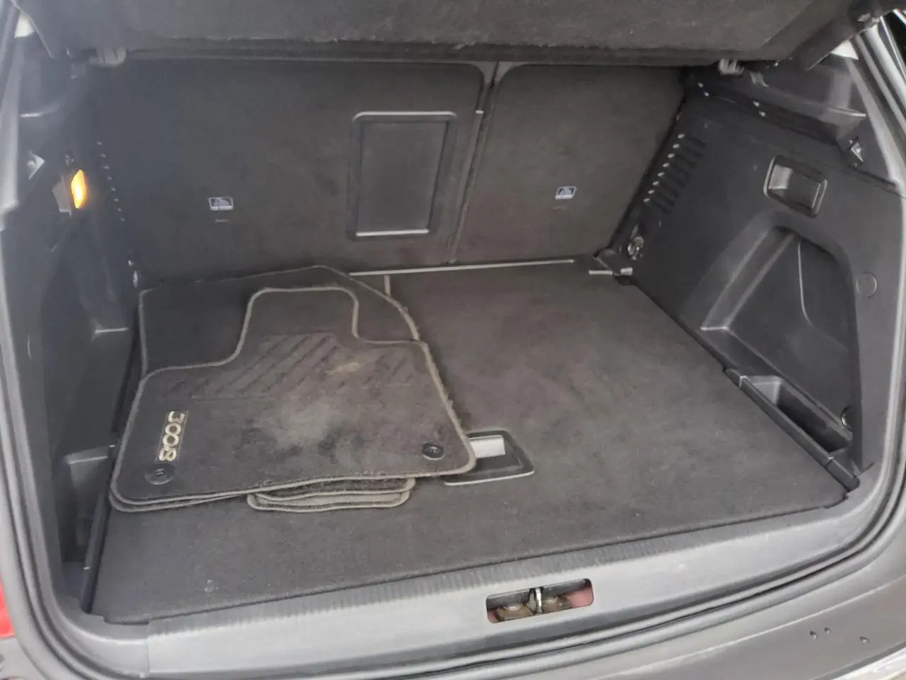 Coffre ouvert d’un Peugeot 3008 rouge foncé, vue intérieure montrant tapis de sol et espace de rangement.