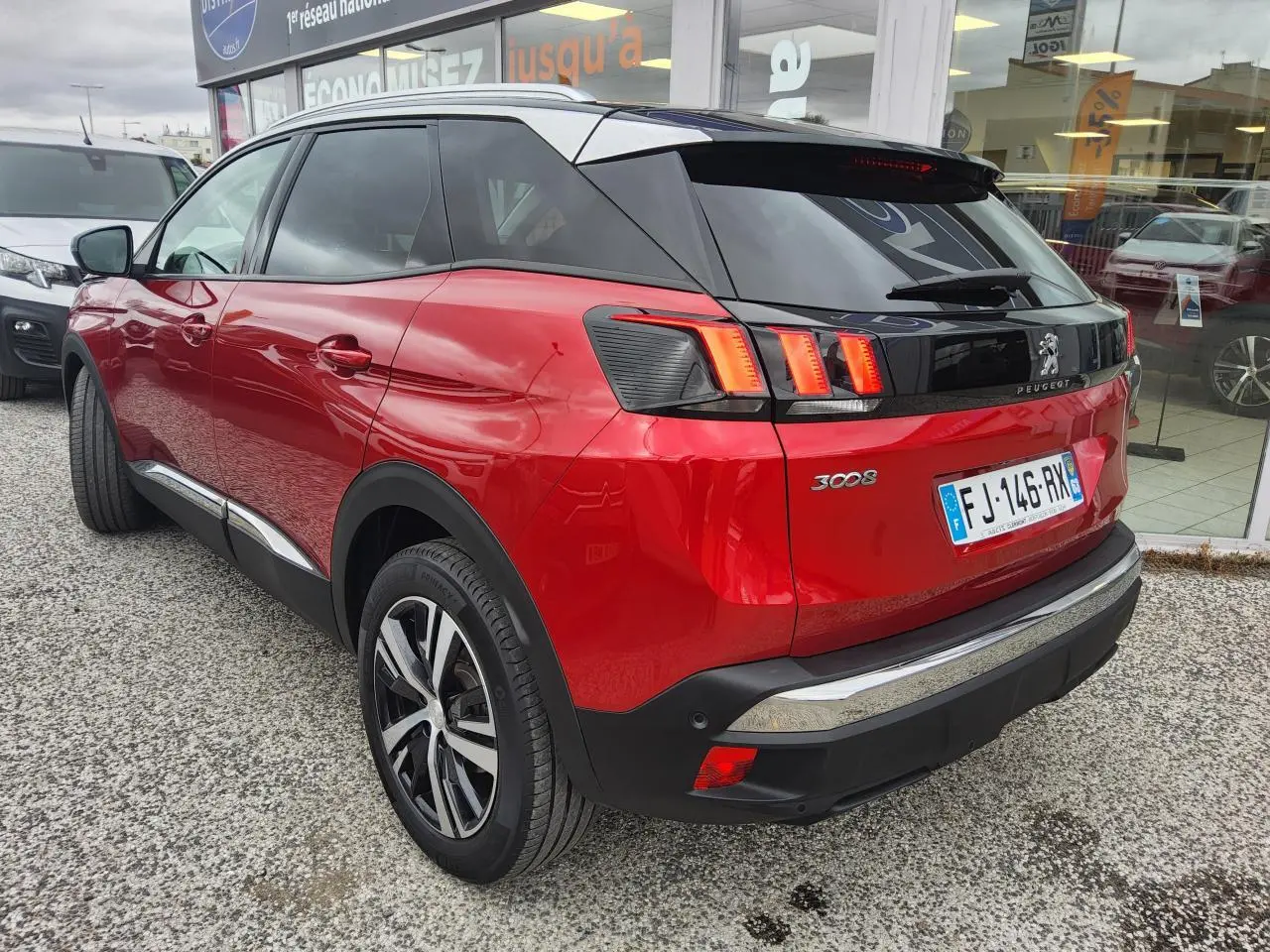 Vue 3/4 arrière droite d’un Peugeot 3008 rouge foncé avec toit noir et jantes alliage bi-ton, garé devant un showroom.