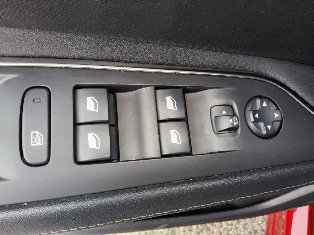 Gros plan sur les commandes des vitres et rétroviseurs côté conducteur du Peugeot 3008 rouge foncé, intérieur noir.