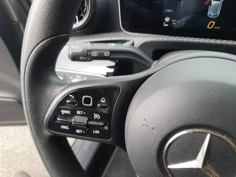 Gros plan sur le volant cuir multifonction côté gauche d'une Mercedes Classe A 160 gris montagne avec commandes de régulateur de vitesse.