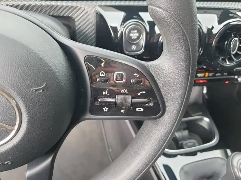 Gros plan sur les commandes multifonctions du volant cuir d'une Mercedes Classe A 160 Style Line 2018, intérieur noir.