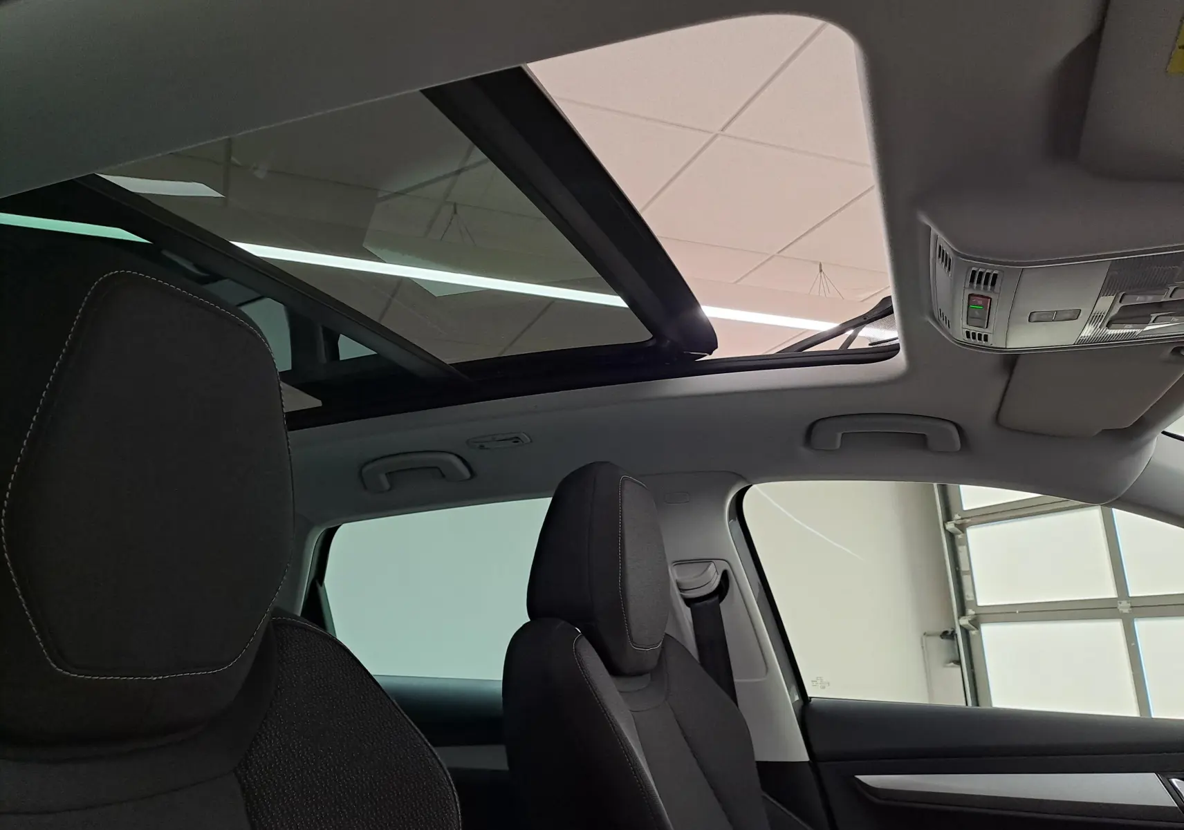 Vue intérieure du toit ouvrant panoramique du Skoda Karoq 2023, avec sièges avant en tissu noir et ciel de toit clair.