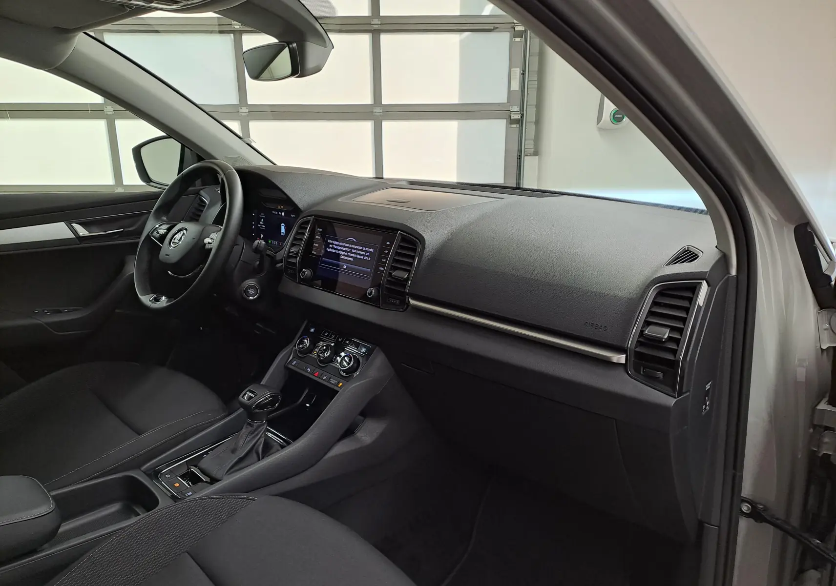 Vue intérieure côté conducteur du Skoda Karoq gris perle 2023, mettant en valeur le tableau de bord digital et la console centrale.