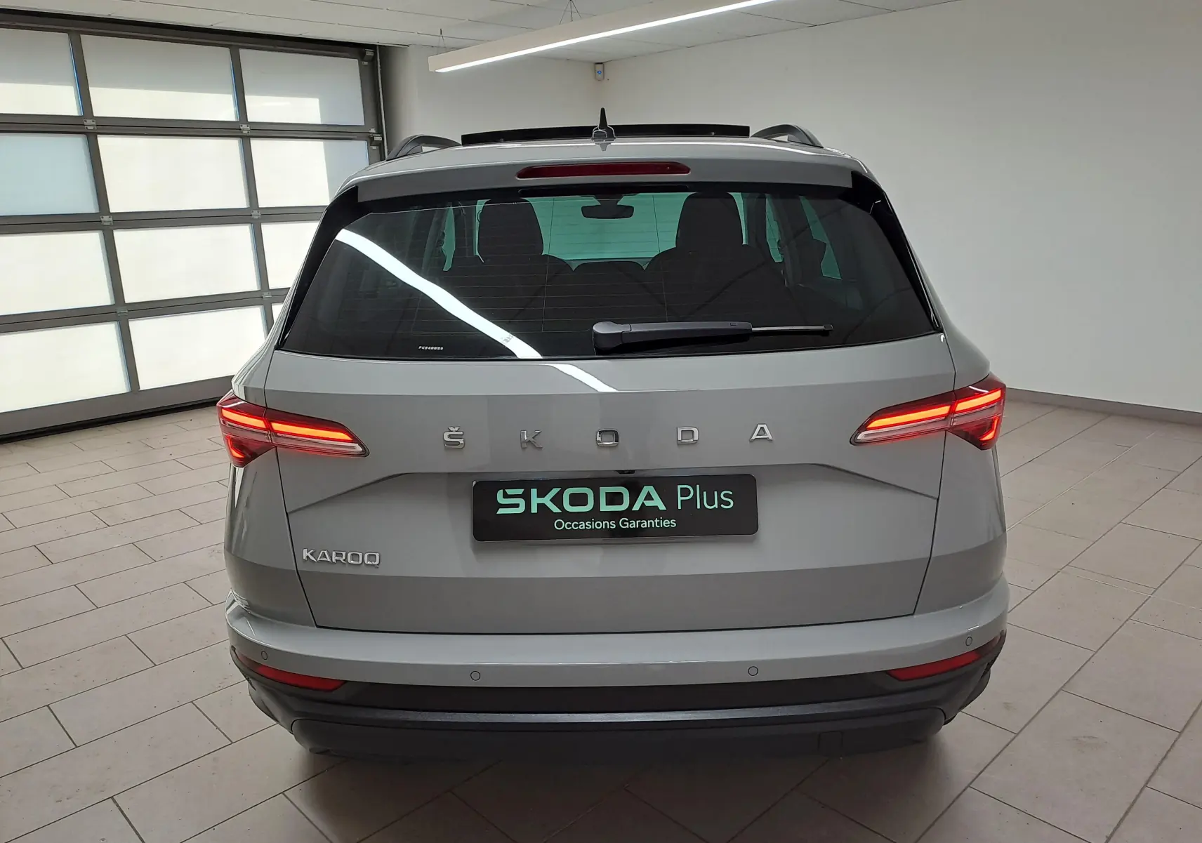 Vue arrière d'un Skoda Karoq gris perle 2023 avec feux allumés dans un garage lumineux.