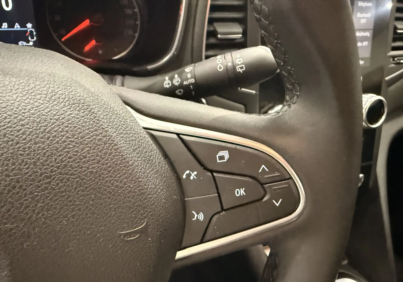 Gros plan sur les commandes au volant en cuir noir de la Renault Mégane IV gris Highland, avec affichage du tableau de bord en arrière-plan.