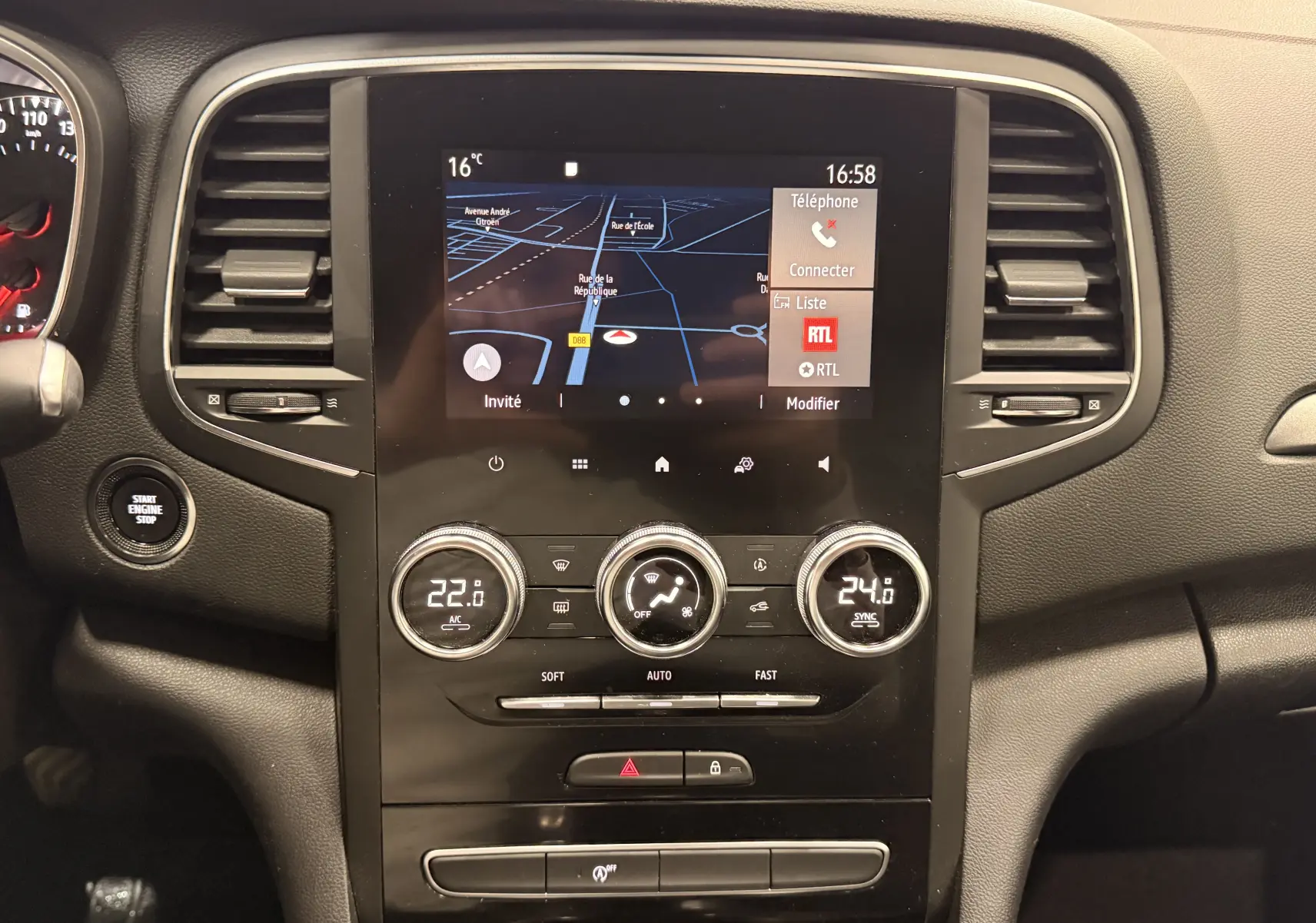 Vue rapprochée du tableau de bord noir de la Renault Mégane IV avec écran tactile et commandes de climatisation digitales.
