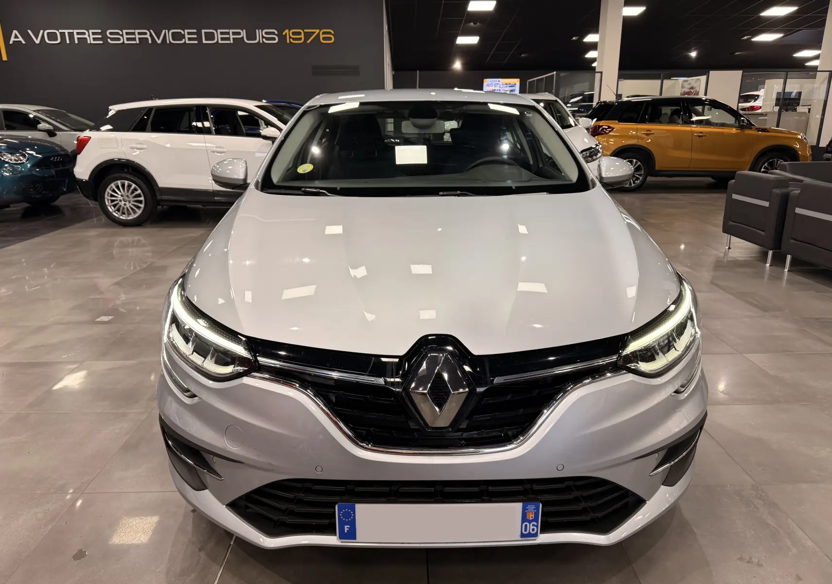 Vue de face d'une Renault Mégane IV gris Highland avec phares LED allumés dans un showroom.