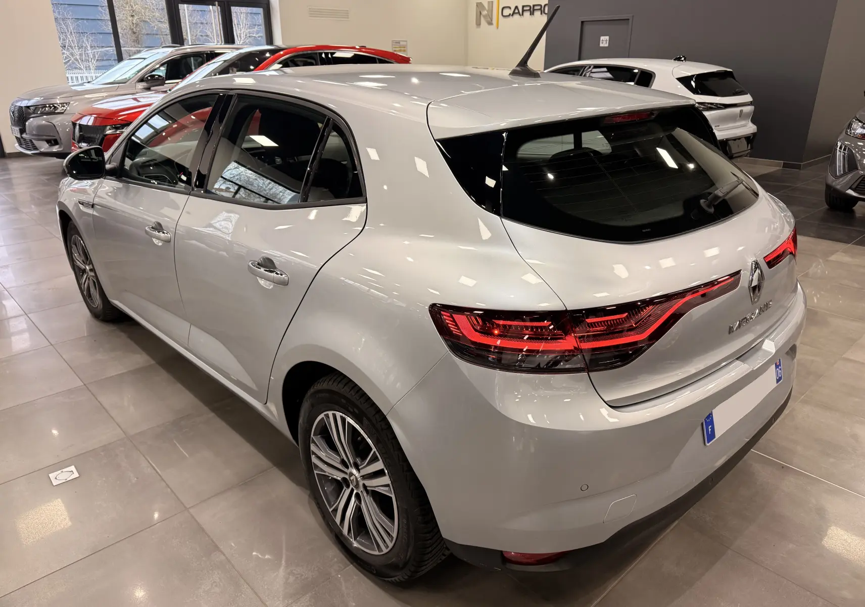 Vue 3/4 arrière droite d'une Renault Mégane IV gris Highland, avec feux arrière LED allumés en concession.