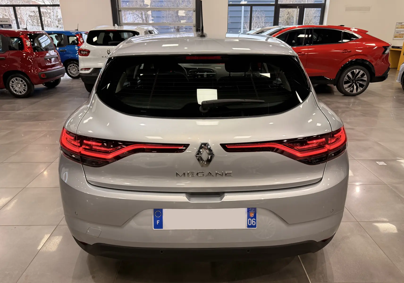 Vue arrière d'une Renault Mégane IV gris Highland avec feux arrière LED allumés dans un showroom.