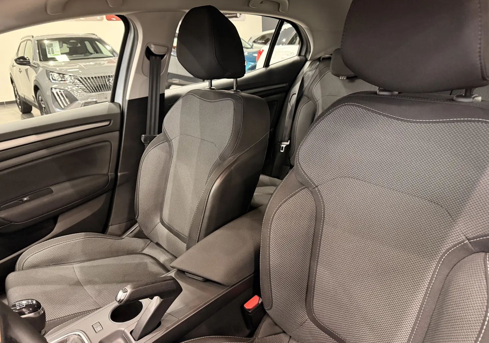 Vue intérieure de la Renault Mégane IV 1.5 dCi 115 gris Highland, montrant les sièges avant en tissu et la console centrale.