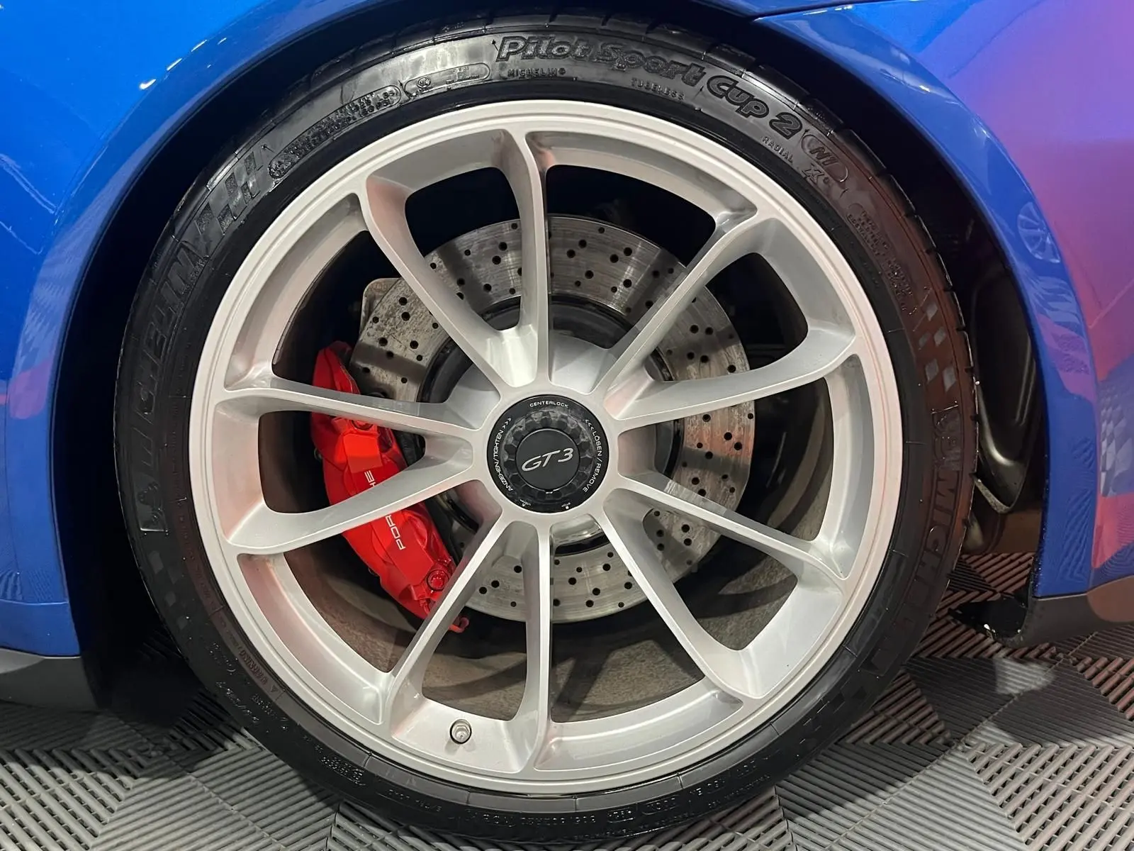 Gros plan sur la roue avant droite de la Porsche 911 GT3 bleu saphir avec étrier de frein rouge et jante argentée.
